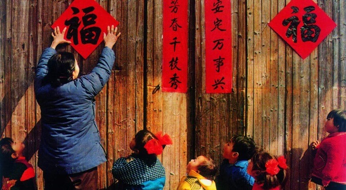 A person sticking Chinese posters on wooden wall along with few kids. 